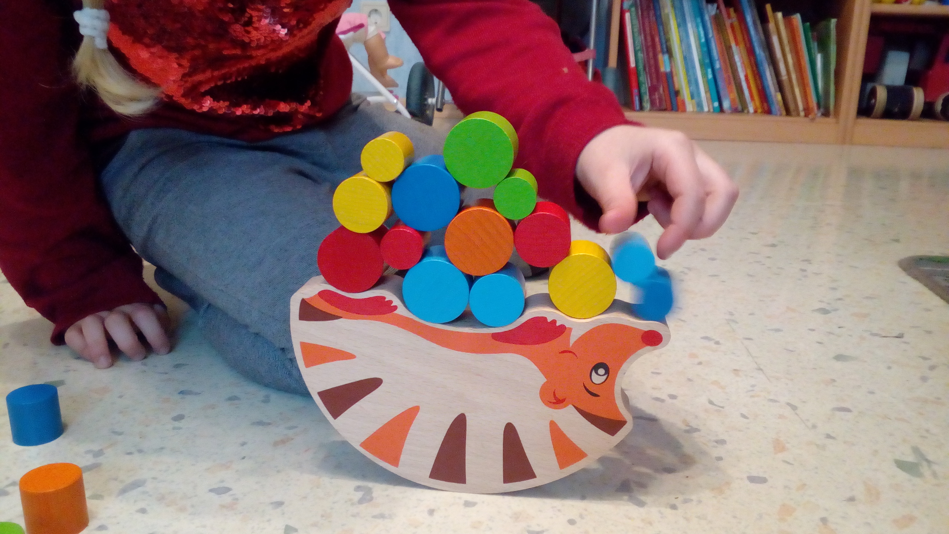 Ein Kind stapelt Bauklötze auf einem Holzigel, dessen Unterseite rund ist, sodass die Klötze gut ausbalanciert werden müssen, damit er nicht umfällt